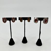 Photo showing all three pairs of earrings on black stands against white background for full lot overview.