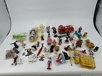 Photo of all toys spread on white surface showing diversity of small vintage toys including cartoon figurines, vehicles, and novelty items.