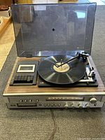 Overall view of the Sears stereo system showing the turntable with a vinyl record and cassette deck with control buttons, woodgrain top and dust cover open.