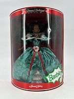Front view of sealed Holiday Barbie doll in red cylindrical display case showing the doll dressed in green and silver Victorian-style gown with holiday decorations.
