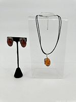 View of earrings on black stand and pendant hanging on clear acrylic block necklace display, showing set together.