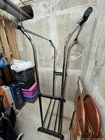 Whole view of the empty adjustable double clothes rack in storage area, showing chrome frame and black plastic joints, bottom rack with four metal rods.