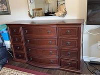 Front view of Bombay Company wooden 12-drawer dresser with curved center drawers and metal handles.