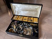 Full view of a large box filled with assorted costume jewellery including necklaces and earrings, with organizational compartments on the lid containing earrings and small pieces.