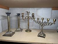 Front view of all four brass candleholders showing the pair of candlesticks with Corinthian tops on the left, the three-arm eagle candelabra in the middle, and the seven-arm ornate candelabra on the right.