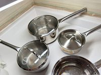 Three stainless steel pots with handles and lids displayed on a kitchen counter.