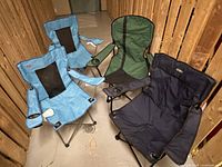 Four folding camping chairs: two light blue matching chairs with black mesh backrests, one green chair with black panel and a small hole in seat, one navy blue padded chair with cup holder.