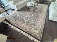 Full view of black and beige floral rug under living room furniture on hardwood floor.