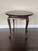 Front view of round mahogany side table showing cabriole legs and scalloped apron.