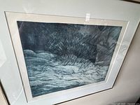 Framed winter landscape print showing snow and bushes in dark tones.