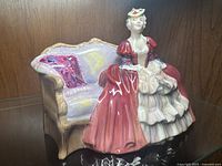 Full view of Royal Doulton Belle of the Ball figurine sitting on a decorated couch with a pink cushion.