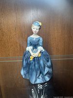 Front view of Royal Doulton figure wearing blue dress and holding yellow gloves and fan