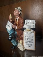 Front and side view of Royal Doulton Stop Press figure showing detailed man with sandwich and newspaper stand.