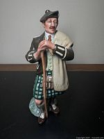 Front angle view of Royal Doulton figure "The Laird" depicting a man in traditional Scottish dress holding a walking stick.