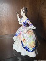 Side angle of Royal Doulton porcelain figurine showing floral painted dress and one arm raised.
