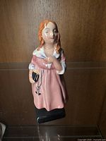 Front angled view of the Royal Doulton Little Nell figurine showing the figurine's red hair, pink dress with white accents, and the book with a key she is holding.