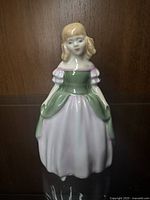 Front view of Royal Doulton Penny figurine showing facial features and dress detail in pink and green.