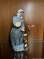 Full side view of the Royal Doulton 'Good Friends' figurine showcasing the woman's blue and gray clothing, tree stump with squirrels, and attached Royal Doulton tag.