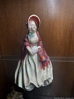 Front and side view of the Royal Doulton porcelain figurine 'Her Ladyship' showing detailed painted red shawl and bonnet.