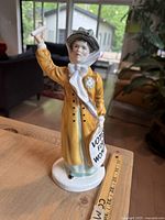Front angle view of the Royal Doulton Votes For Women figurine on wooden surface next to a ruler showing height.