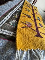 Side angled view showing the yellow wool tapestry with bird motifs and the silk tapestry beneath it