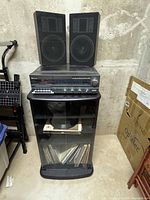 Wide view of stereo receiver on black cabinet with two speakers on top, and vinyl records stored inside cabinet with glass doors.