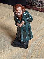 Full view of the Royal Doulton Fagin ceramic figurine standing on a light wooden surface with a carpeted floor background.