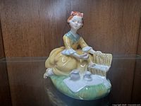 Porcelain Royal Doulton female figurine in yellow dress sitting on grass with picnic items and open basket