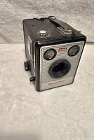 Front angled view showcasing the black body, silver faceplate, dual viewfinders and central lens of the Kodak Brownie Model 1 camera.