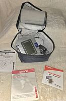 Omron blood pressure monitor in carrying case with arm cuff, power adapter, and instruction manuals displayed.