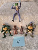 Photo of five collectible figures on beige fur fabric: two Ninja Turtles, two Jawas, and one Joker figure, with a blue paper labeled 'Lot 4'.