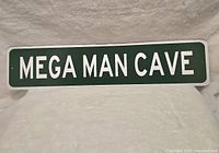 Metal rectangular sign with 'MEGA MAN CAVE' in white text on green background