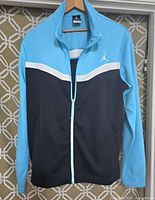 Front view of men's light jacket in black and blue with white stripe and Air Jordan logo