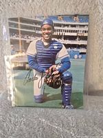 Full view of signed photo showing Carlos Delgado kneeling and smiling in catcher gear at stadium.