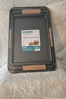 Three stacked cookie baking sheets with packaging label indicating brand and size, new and sealed.