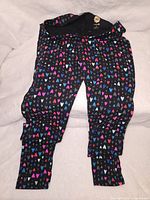 Full length view of the black tights with colorful heart patterns spread throughout the fabric.