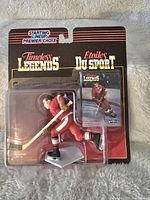 Photo showing new unopened Gordie Howe Starting Lineup Timeless Legends figure in red uniform with hockey stick, sealed in original blister pack with card behind.