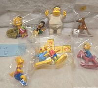 Photo of all seven Simpsons figures individually bagged and arranged for display.