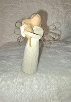 Front view of Willow Tree angel figurine holding a small animal, on a soft textured white surface.
