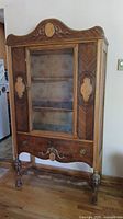 Front view of wooden 3 shelf curio cabinet with decorative inlay and glass door, showing shelves and drawer.