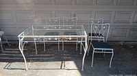 Overall view of set including four matching white metal chairs and glass-top metal frame table on ground in front of garage door
