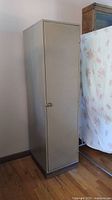 Full view of beige metal locker standing upright on wooden floor against wall.