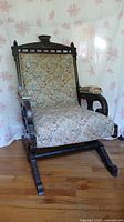 Front view of antique wooden rocking chair with floral upholstered seat and back.