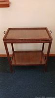Front view of antique wooden rolling tray table with glass top and lower glass shelf