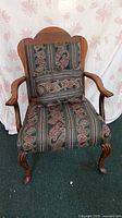 Front view of the antique upholstered armchair showing the patterned fabric seat, backrest, and wooden carved arms and legs.
