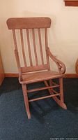 Front view of the antique wood rocking chair showing the slatted backrest and plain seat, with curved armrests featuring scroll details.