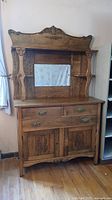 Full view of the antique wooden sideboard showing carved details, two drawers with metal handles, two bottom cupboard doors without handles, and central mirror inlay.