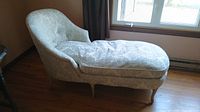 Full side view of the cream chaise longue with high back and removable cushion. The fabric has a floral pattern, and the wooden legs show paint chipping.