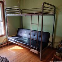 Full view of bunk bed showing metal frame, ladder, top bunk and black faux leather day bed sofa below.