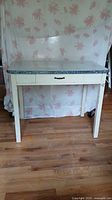 Front view of enamel-topped farm table showing drawer and white legs with paint chipping and peeling.